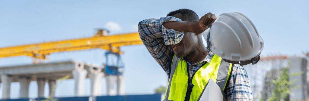 Outdoor construction worker in a high-visibility vest experiencing heat exposure while working alone at a job site