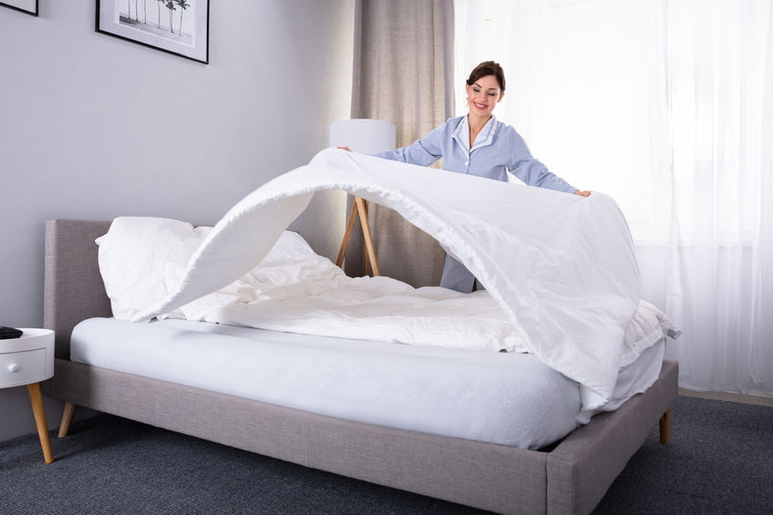 Lone Working Housekeeper Arranging Bedsheet On Bed